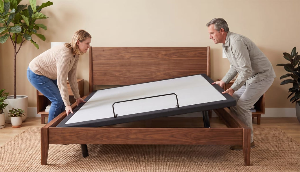 Couple lowering a white adjustable base into a walnut bed frame in a bedroom