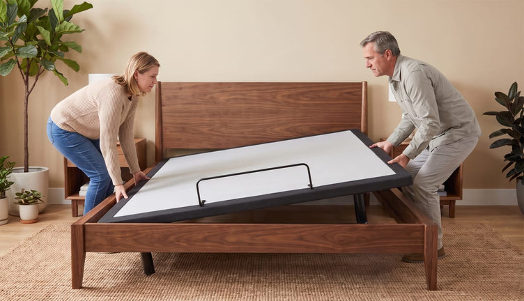 Couple lowering a white adjustable base into a walnut bed frame in a bedroom