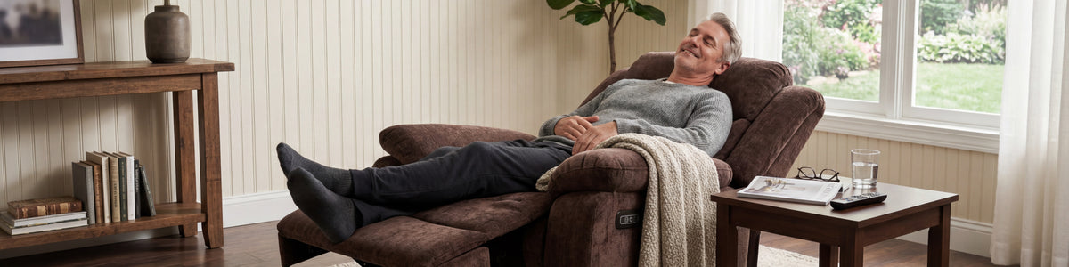 Man relaxing in a fully reclined brown Tami Tami power lift chair in a sunlit living room